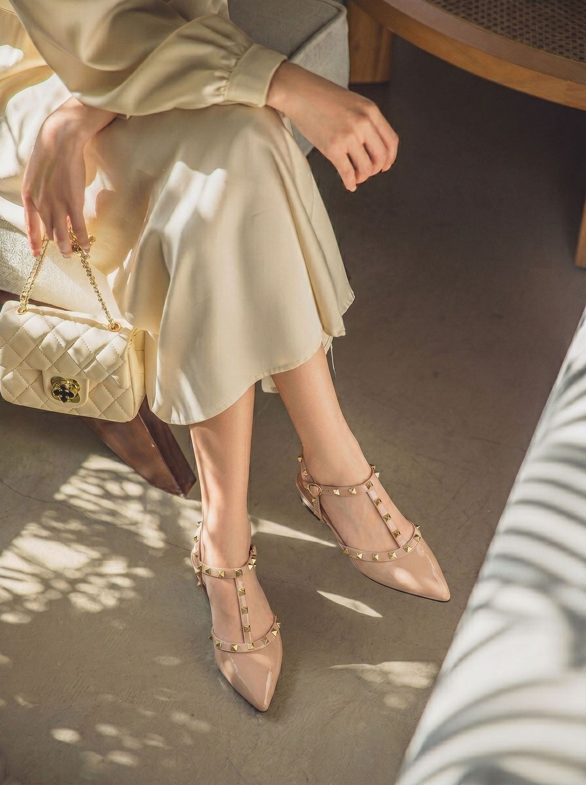 Moncelia beige studded T-strap flats, worn seated with a cream satin skirt, women's sizes 5 to 10.5