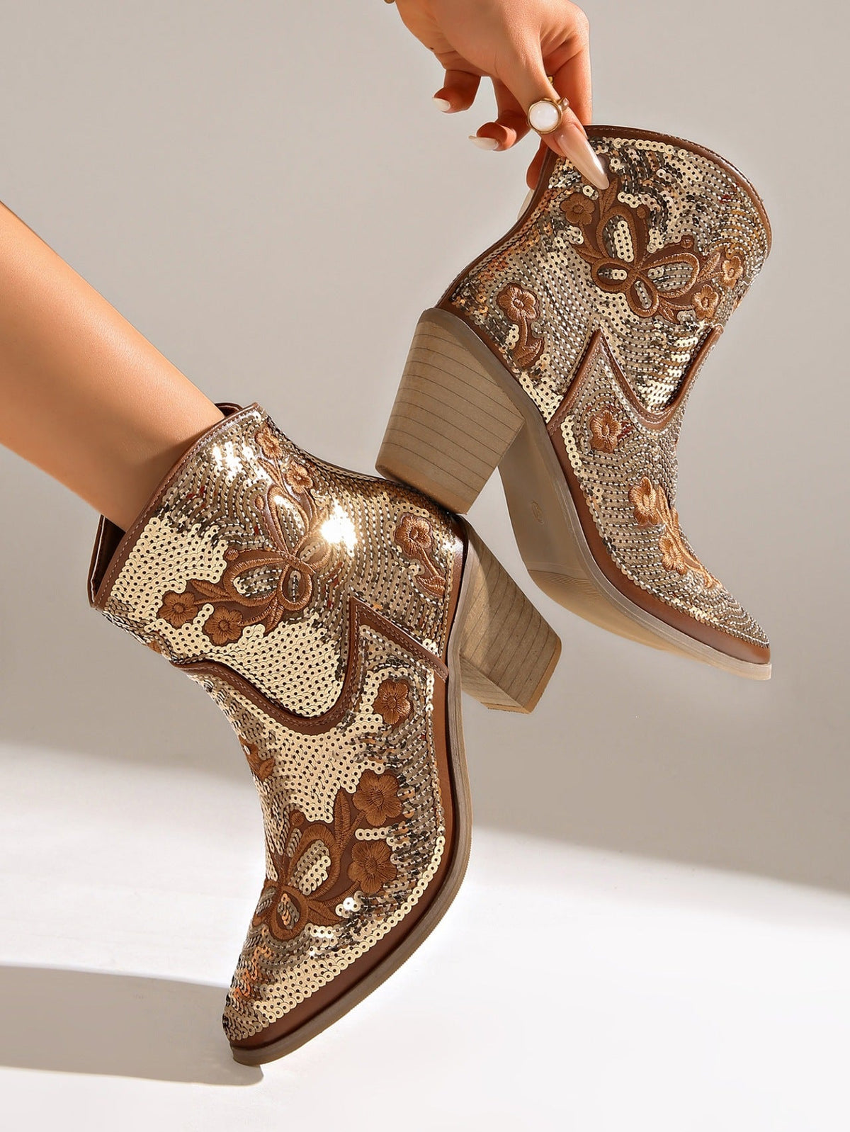 Moncelia gold sequin western ankle boots, held by model showing stacked block heel, women's sizes 5.5 to 12