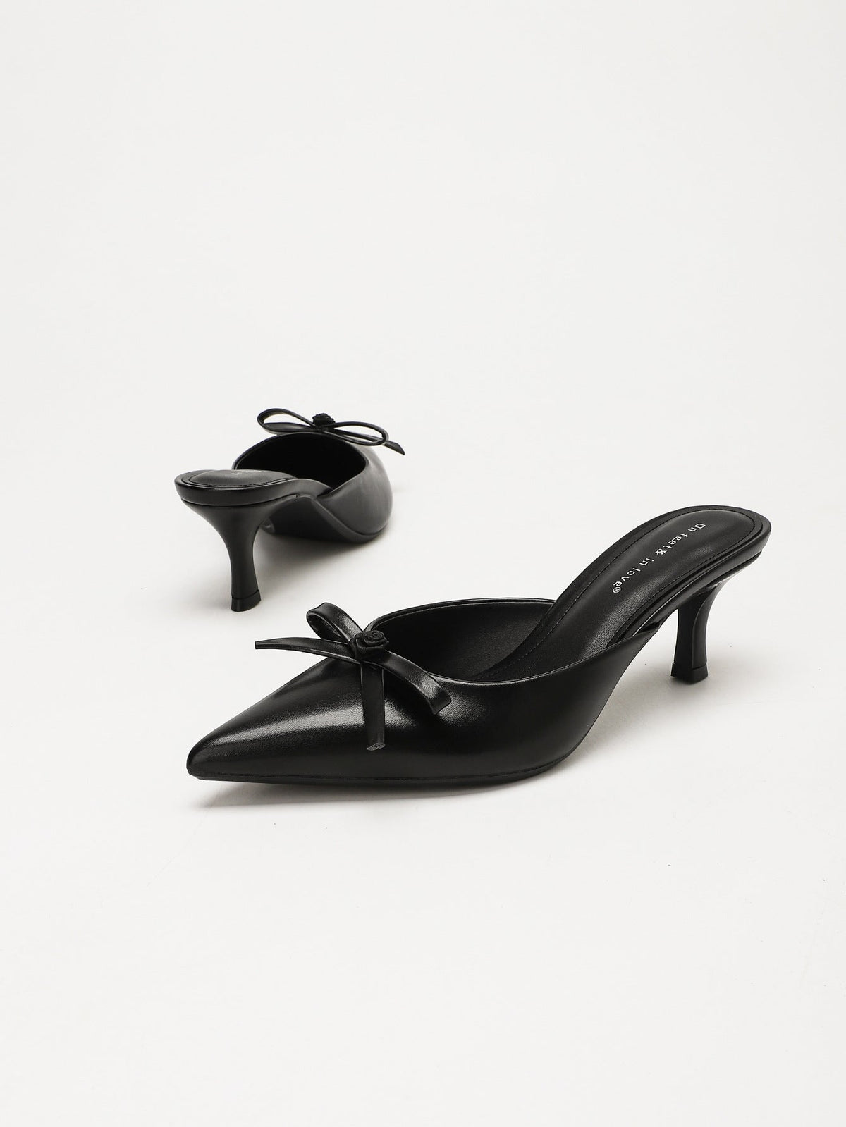 Moncelia black bow pointed toe curved heel mules, pair shown from the side, women's sizes 5 to 11.5