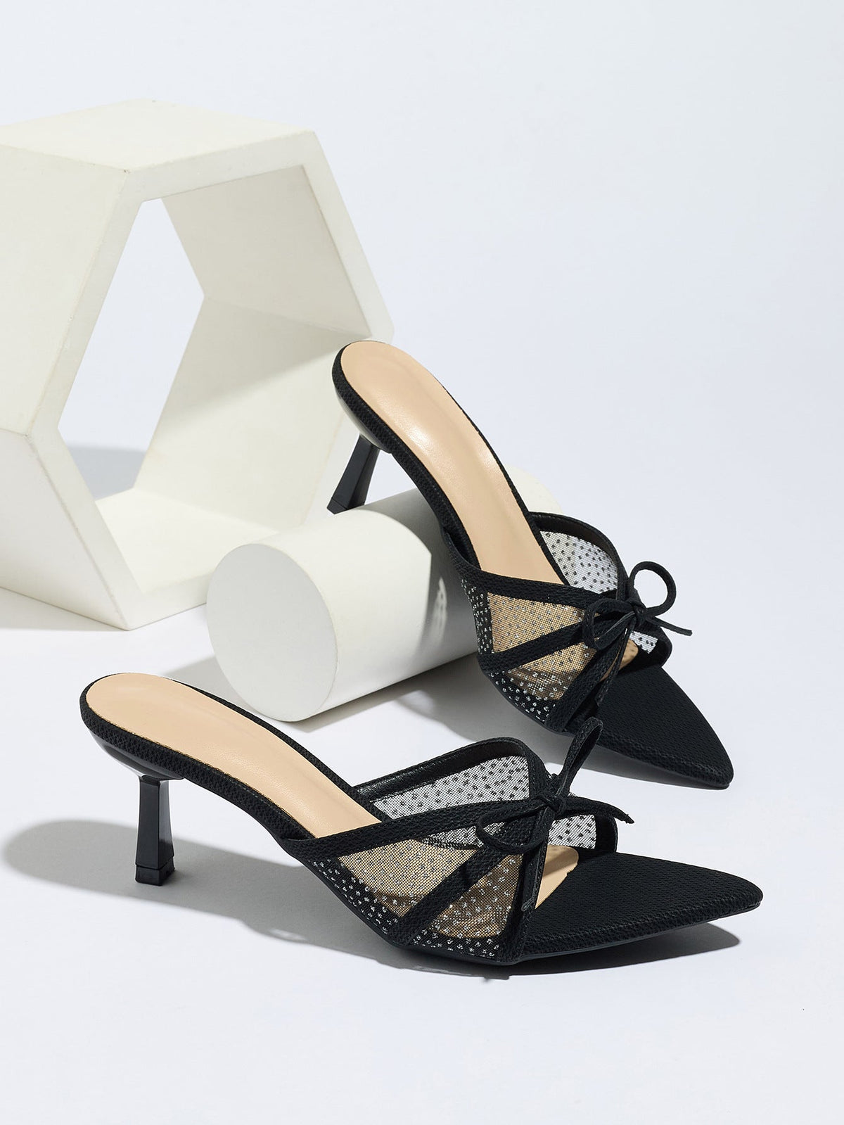 Moncelia black bow mesh pointed toe heeled mules, pair styled on a white display, women's sizes 5 to 12