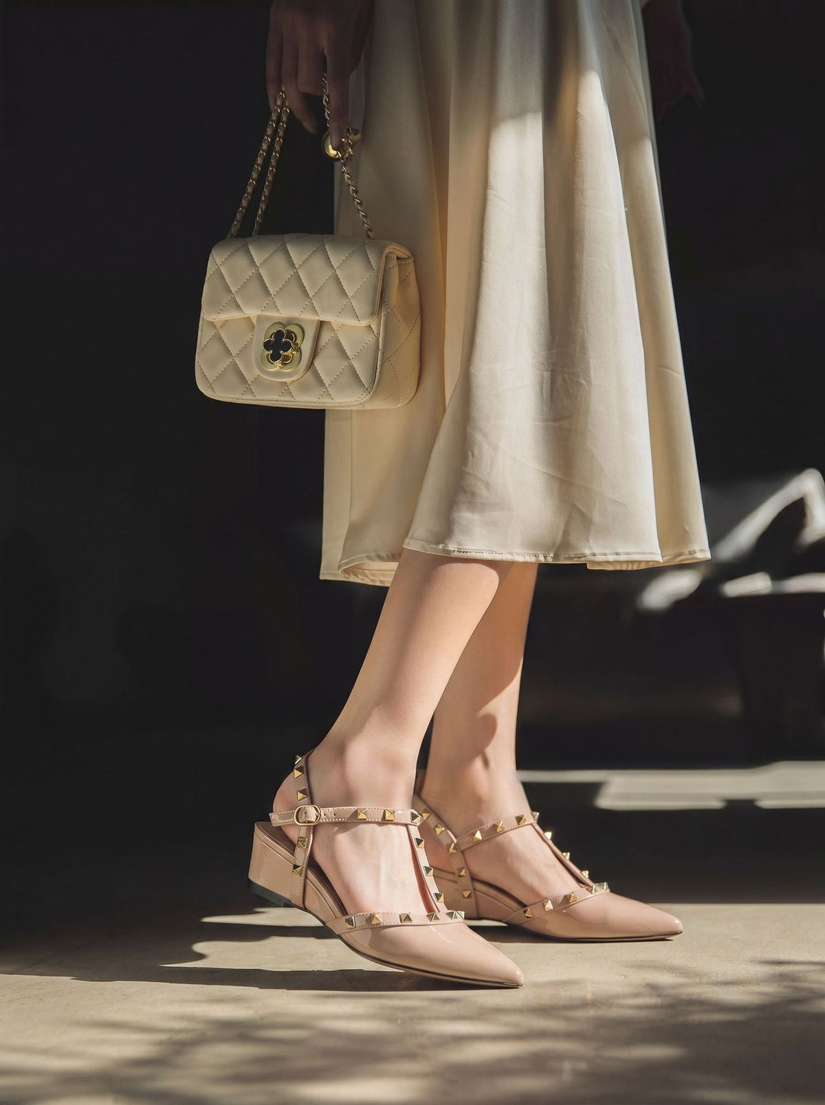 Moncelia beige studded T-strap flats, worn standing with quilted bag and midi skirt, women's sizes 5 to 10.5