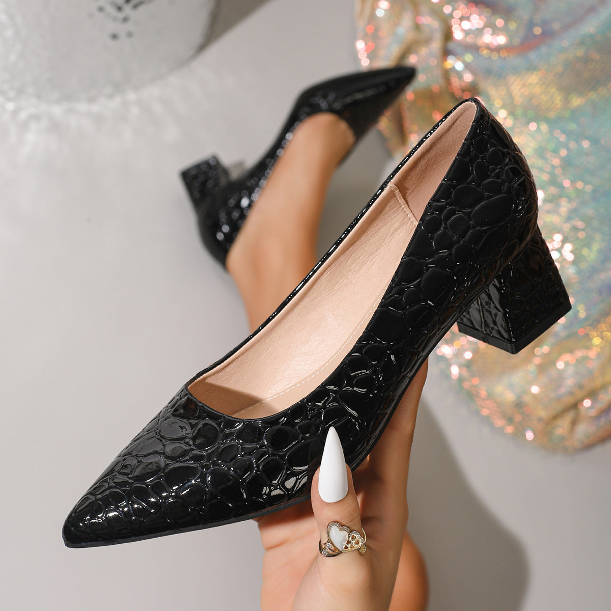 Moncelia black croc-embossed block heel pumps, held in hand showing croc texture, women's sizes 5.5 to 12