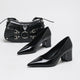 Moncelia black high-shine block heel pumps, pair shown with a studded black handbag, women's sizes 5 to 11.5