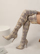 Moncelia cream snake print over-the-knee boots, worn seated showing stiletto heels, women's sizes 5.5 to 9