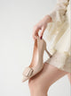 Moncelia beige folded plate pointed toe pumps, close-up held in hand by the heel, women's sizes 5.5 to 10.5