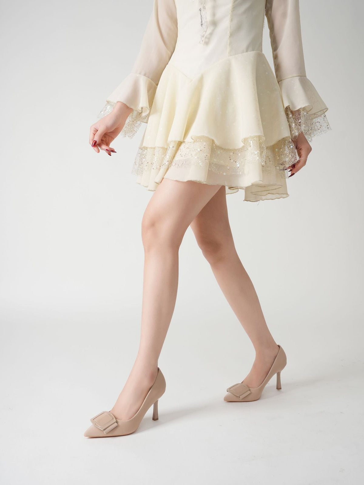 Moncelia beige folded plate pointed toe pumps, front view on model mid-step, women's sizes 5.5 to 10.5