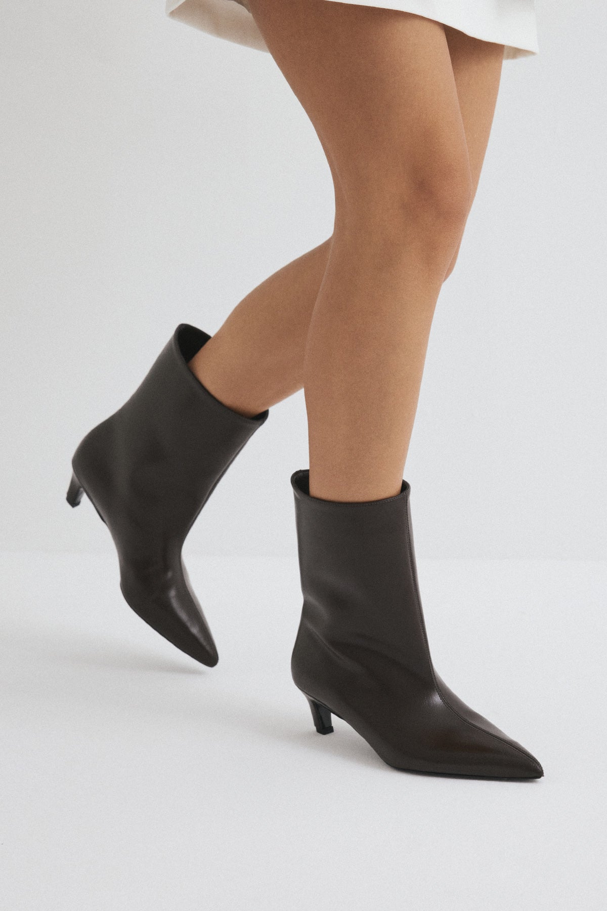 Moncelia brown pointed toe kitten heel booties, side view on model mid-step, women's sizes 5 to 12