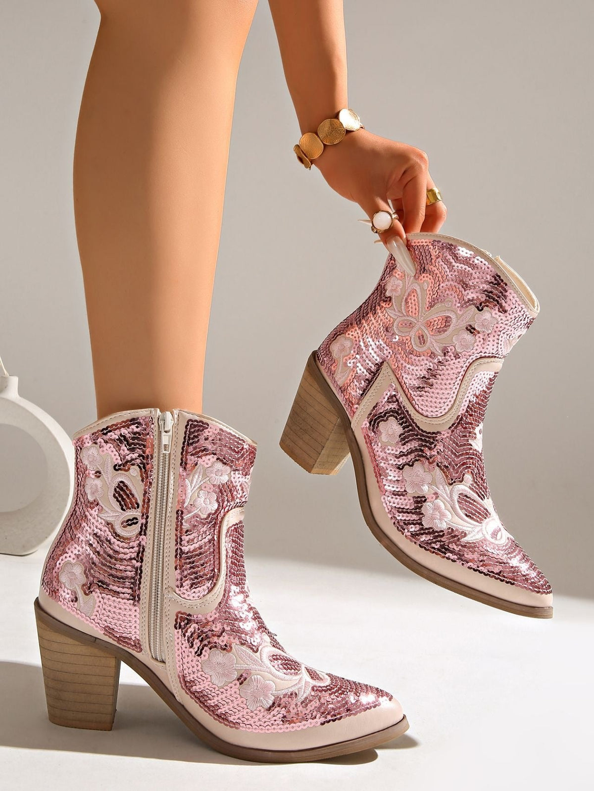 Moncelia pink sequin western ankle boots, worn and held by model showing the heel, women's sizes 5.5 to 12