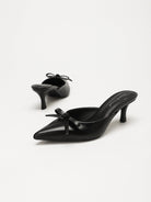 Moncelia black bow pointed toe curved heel mules, pair shown from the side, women's sizes 5 to 11.5