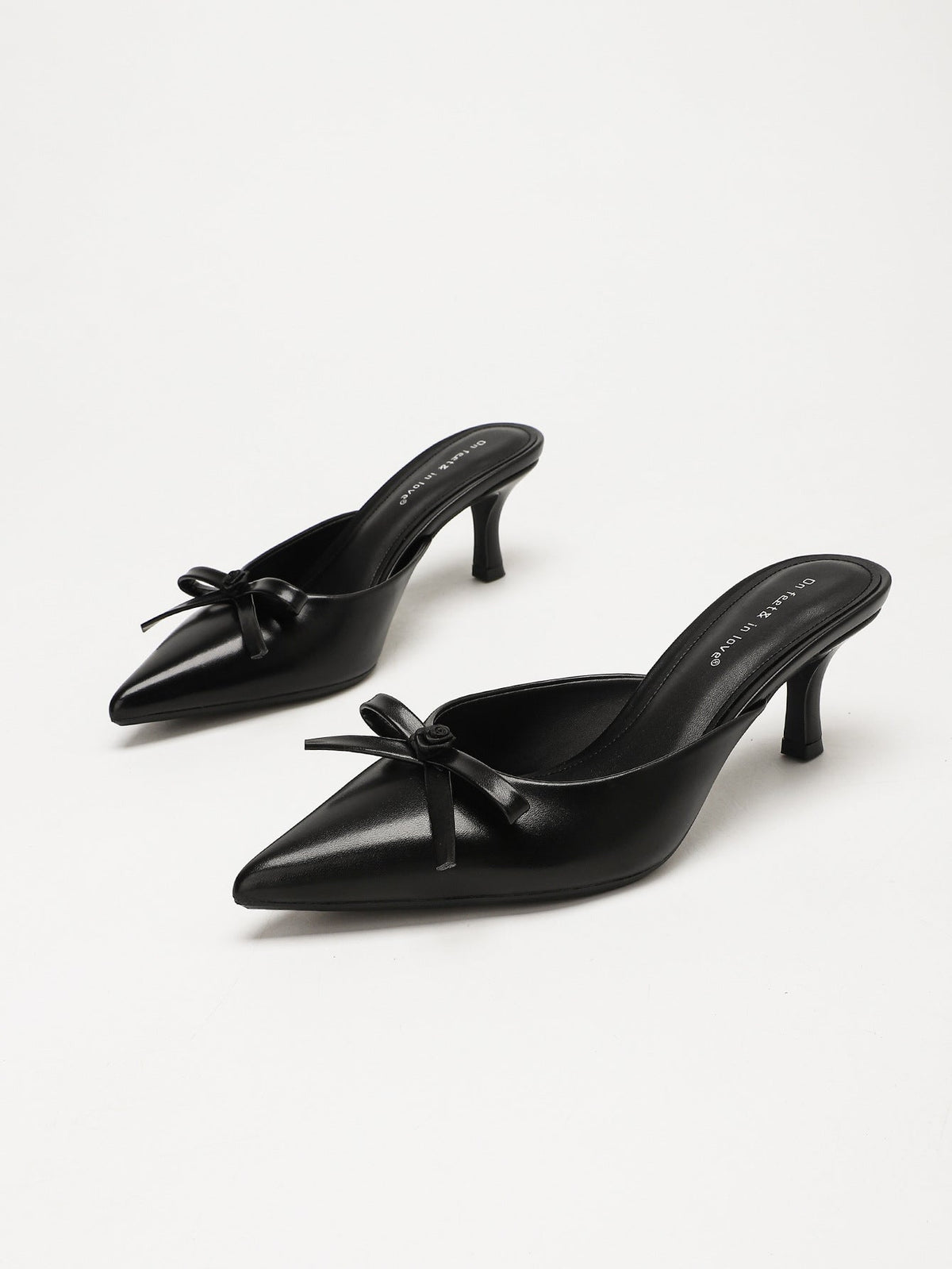 Moncelia black bow pointed toe curved heel mules, pair shown at an angle showing bow, women's sizes 5 to 11.5