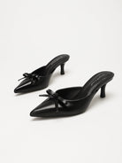 Moncelia black bow pointed toe curved heel mules, pair shown at an angle showing bow, women's sizes 5 to 11.5